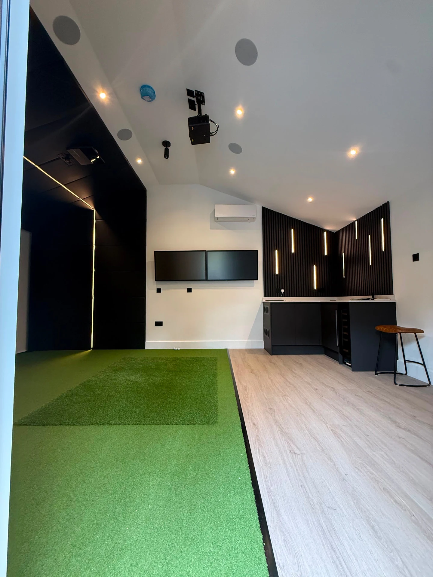 Golf simulator interior showing ceiling projection, integrated audio, lighting and a padded screen enclosure