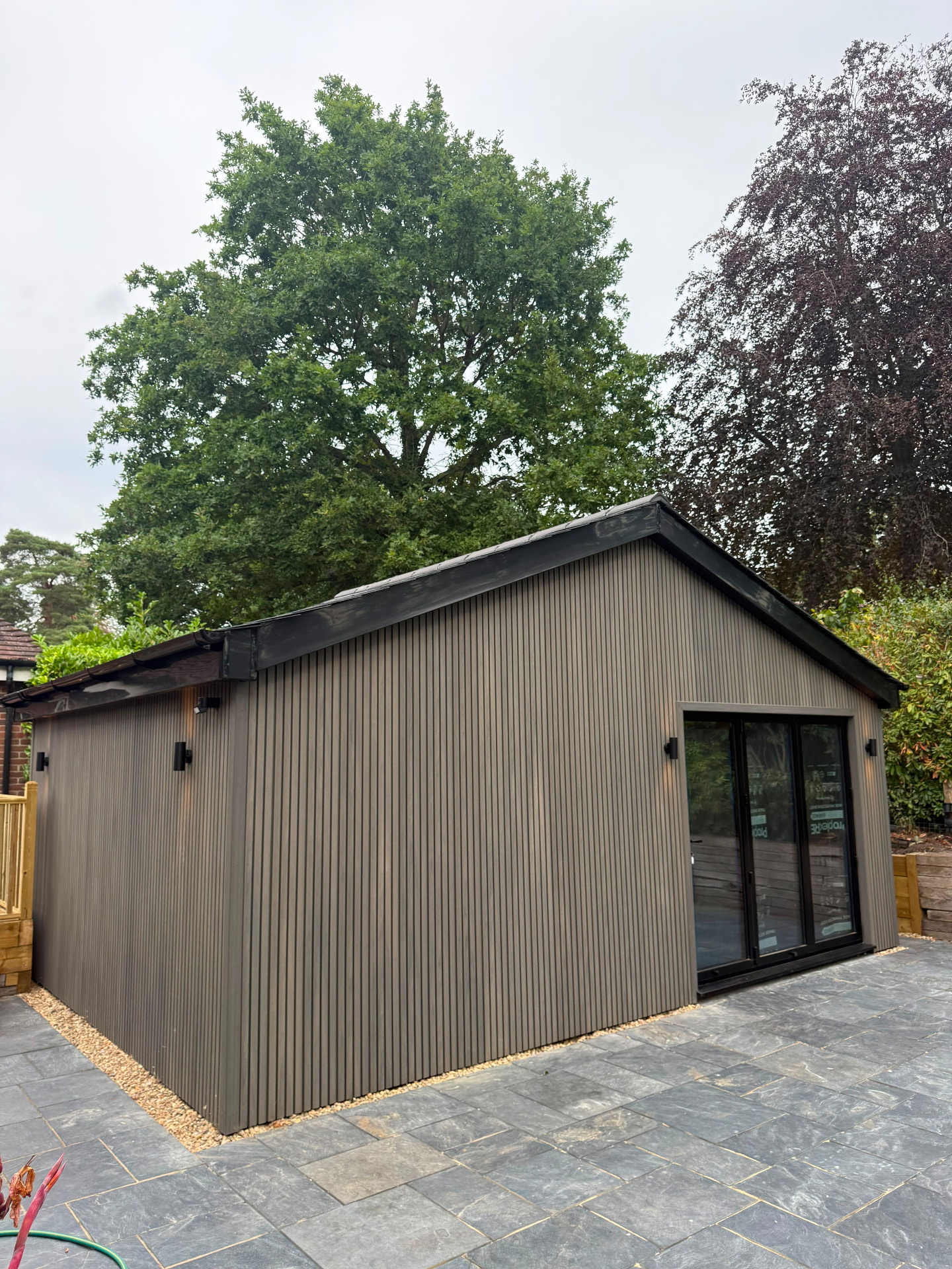 Bespoke dark-clad garden building with glazed doors and a landscaped approach