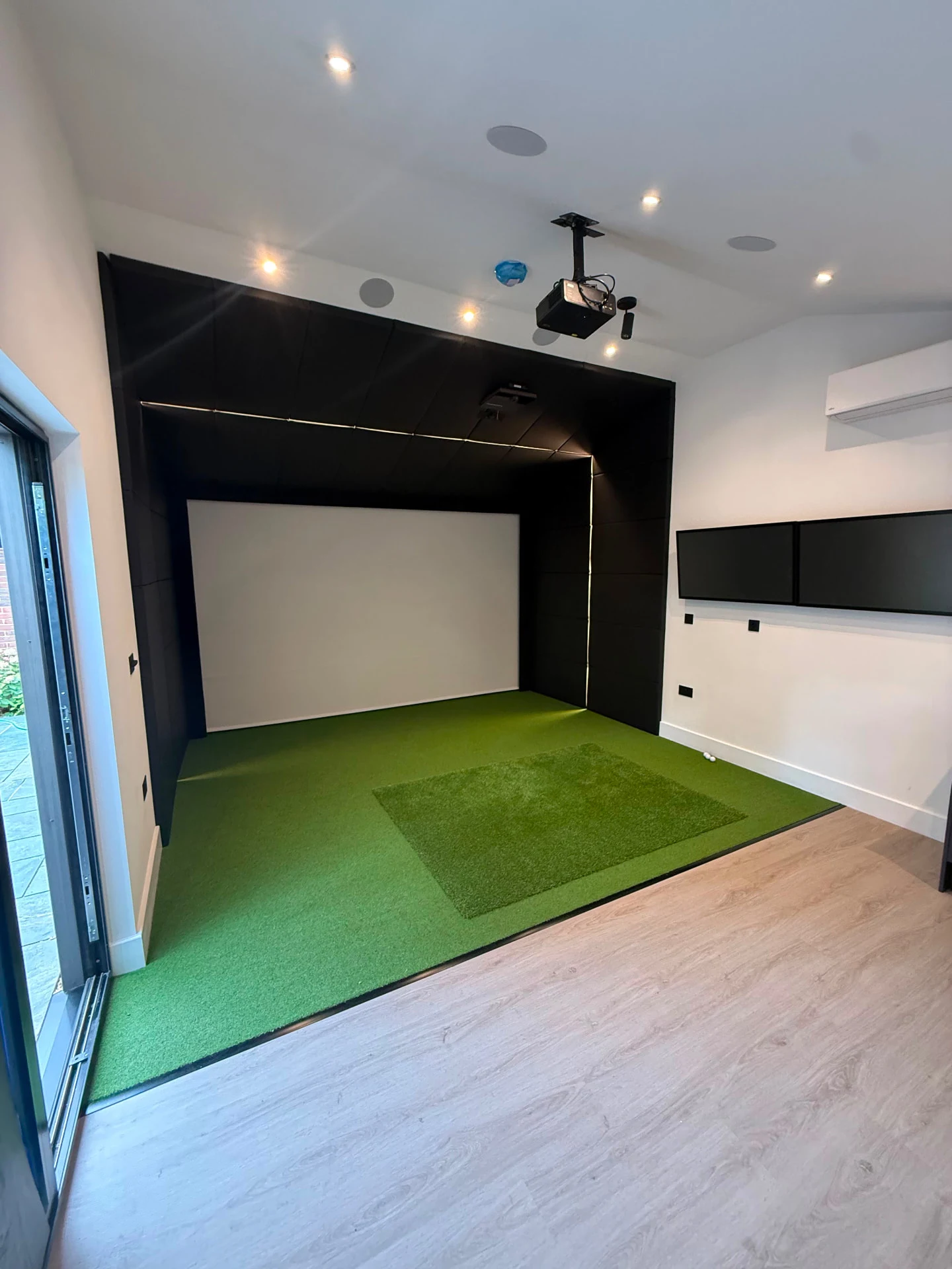 Single golf simulator bay with padded enclosure, hitting turf and integrated ceiling equipment